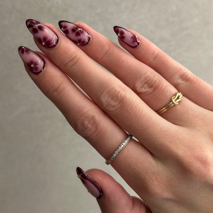 Hand with maroon nail polish and multiple rings on a neutral background